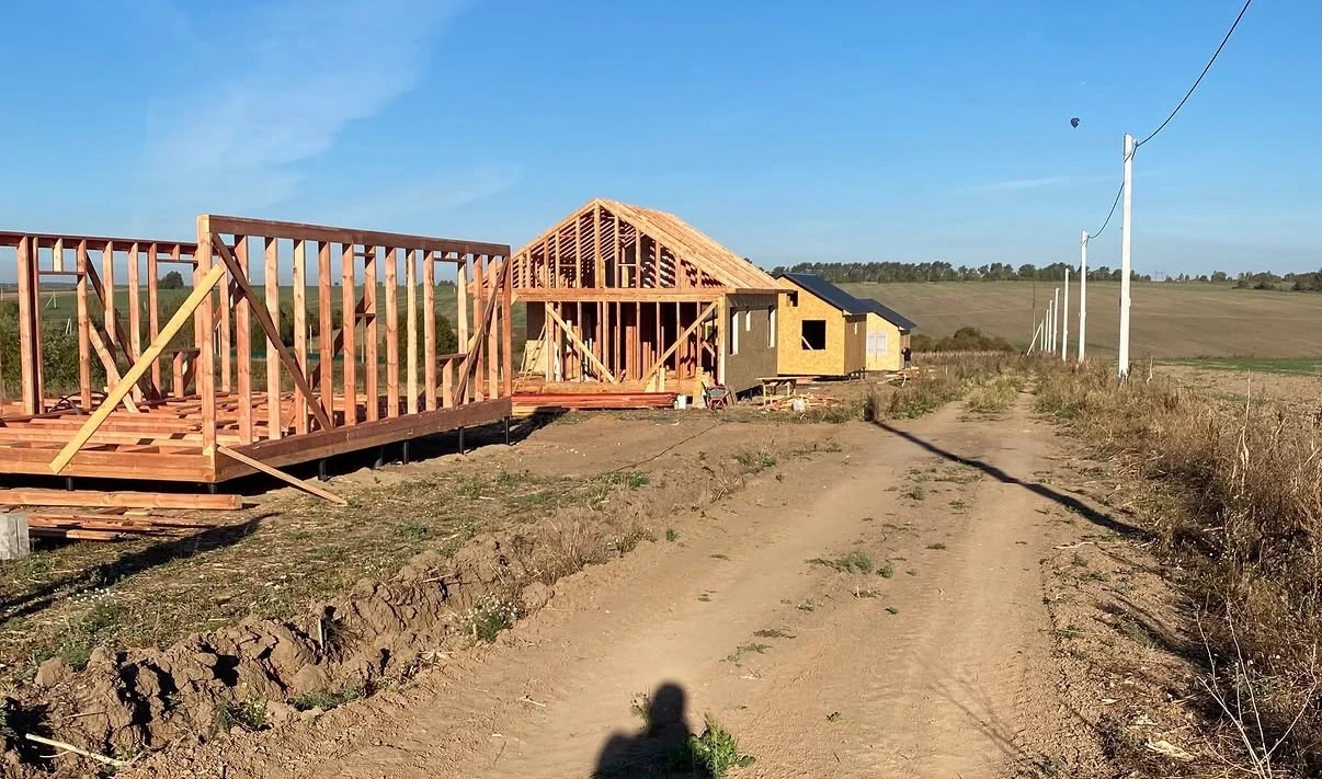 Two timber-frame houses under construction on a plot by the access road