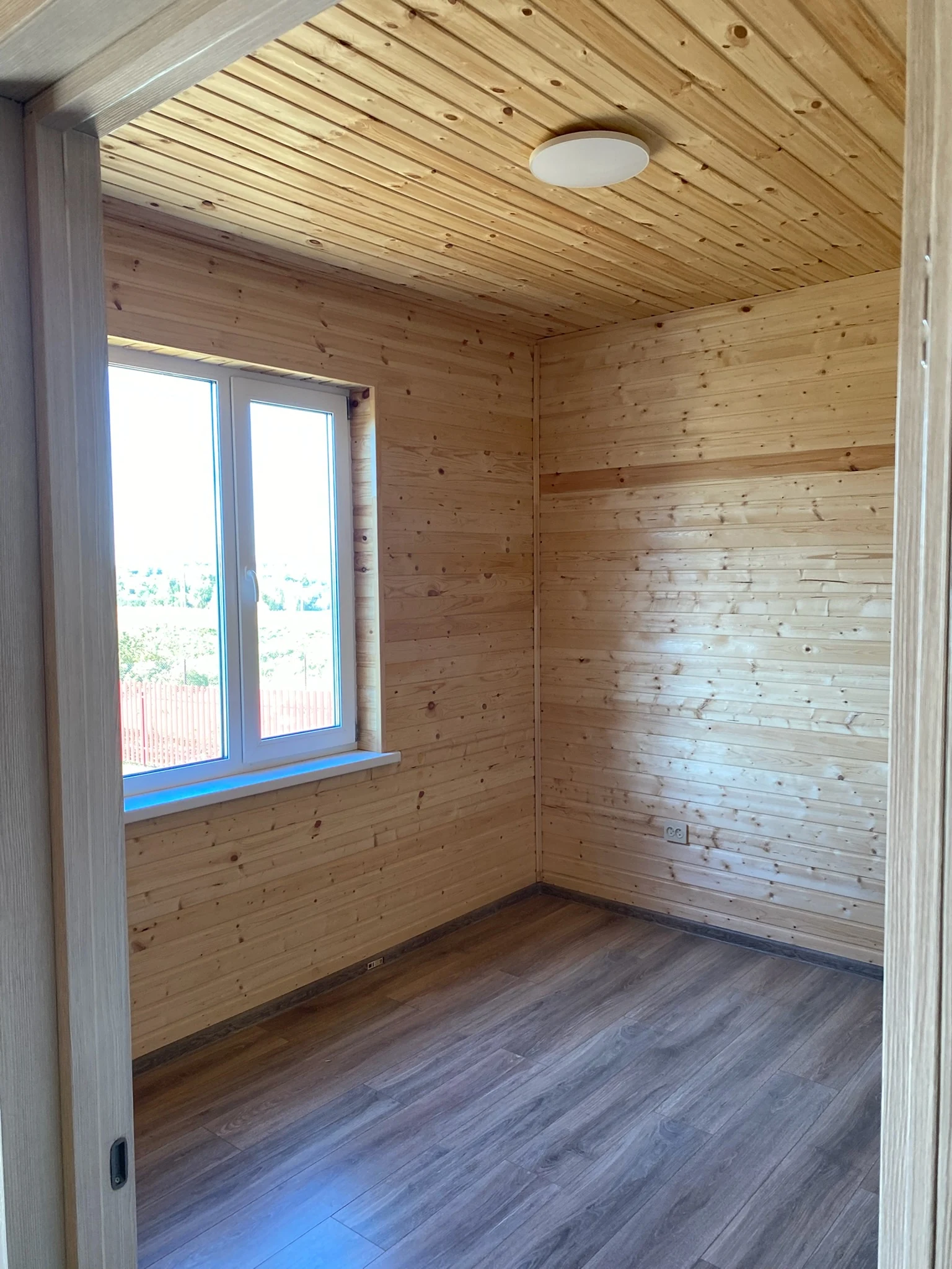 Room lined with pine boards, with a window and laminate flooring