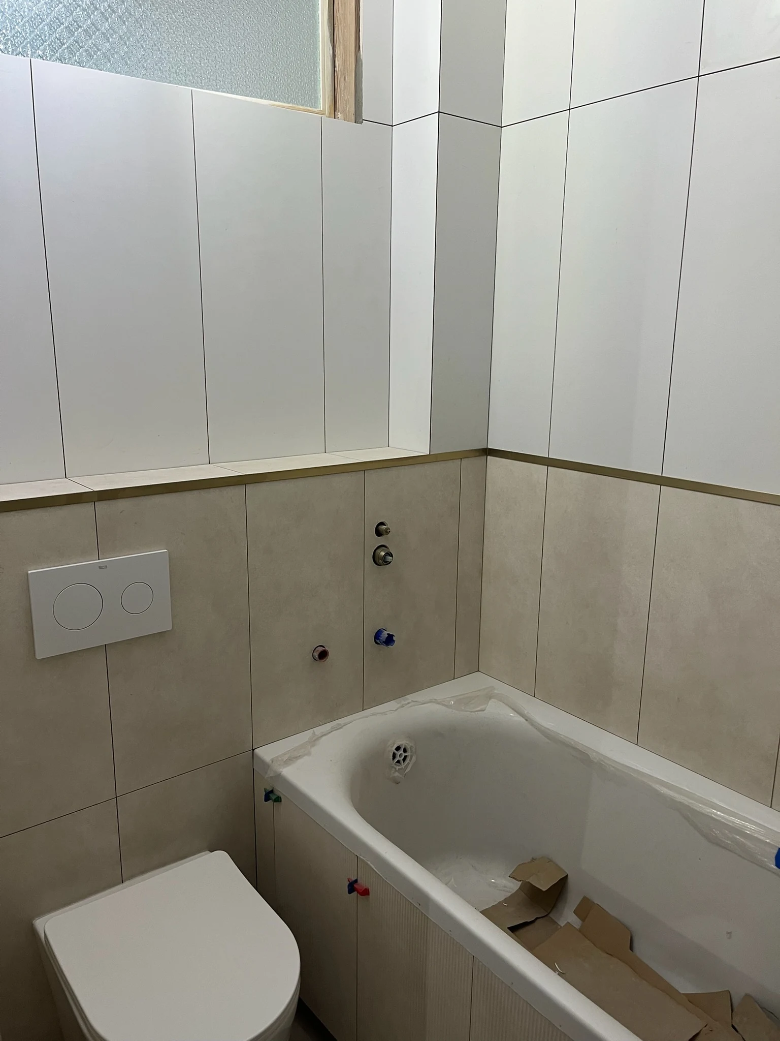 The same bathroom after tiling, with a built-in bathtub and a wall-hung toilet