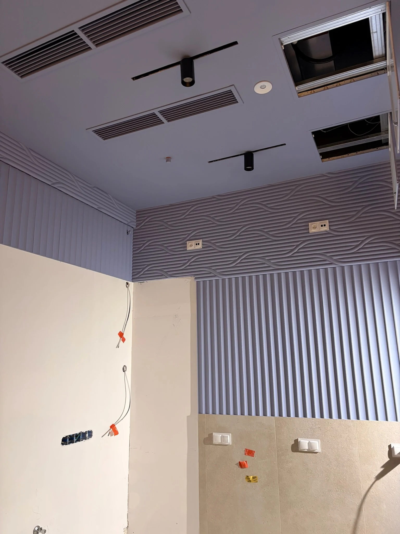 Wall with 3D panels and a suspended ceiling with air vents and lighting tracks