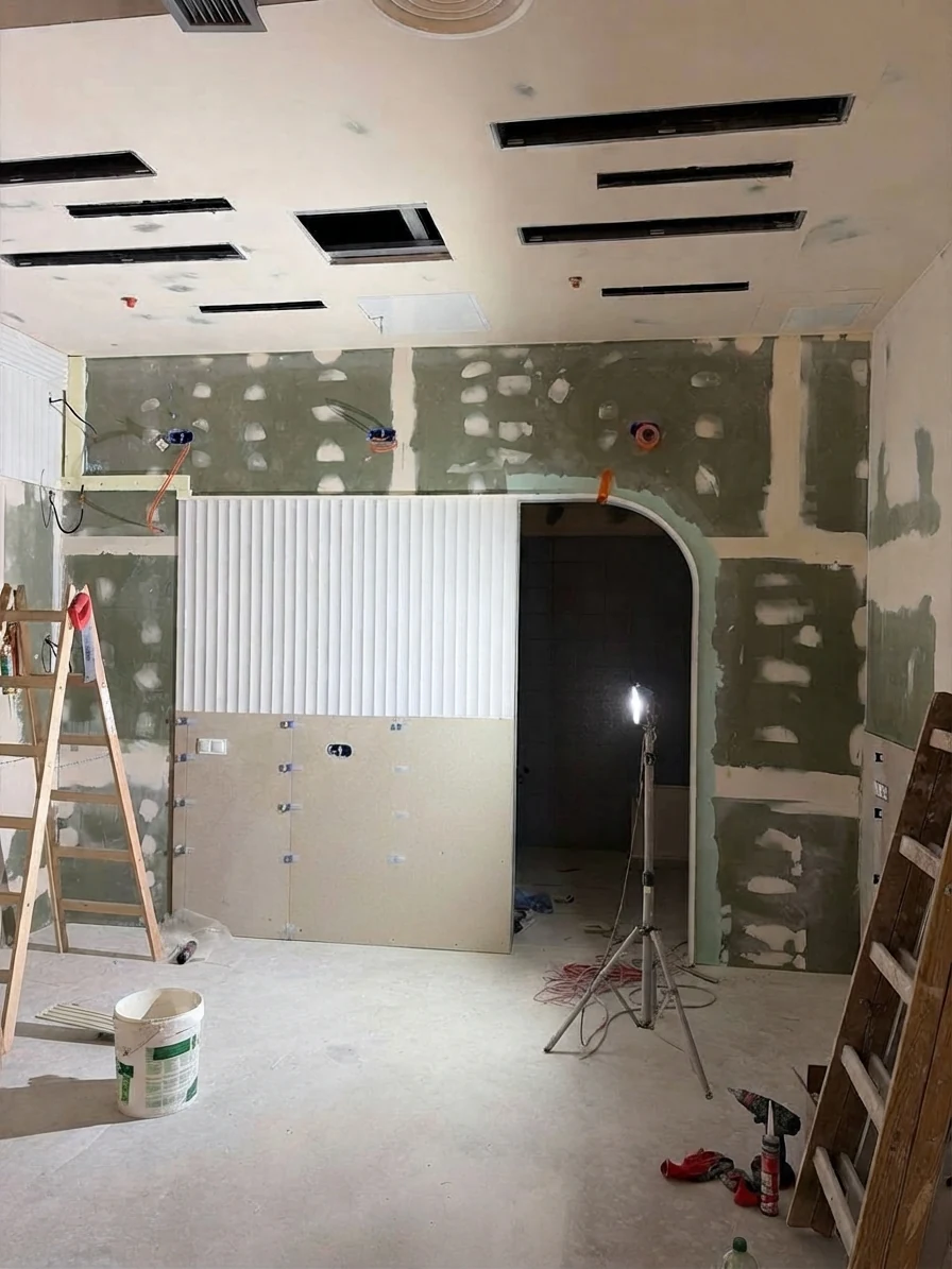 The space in its raw state: an arched opening in bare plasterboard, ladders and a work lamp